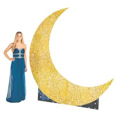 a woman in a blue dress standing next to a large yellow crescent shaped object with stars on it