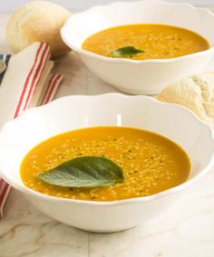 two white bowls filled with soup on top of a marble counter next to bread and a napkin