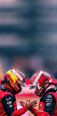 two men in red racing uniforms standing next to each other with helmets on their heads