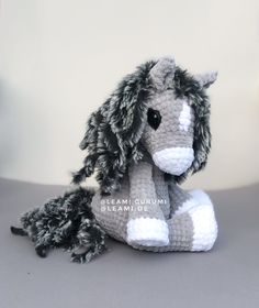 a crocheted gray and white horse sitting on top of a grey table next to a wall