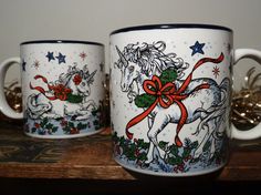 two coffee mugs sitting on top of a wooden table with christmas decorations and bows