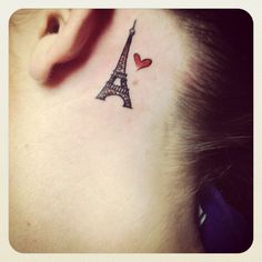 a woman with a small tattoo on her neck and behind her ear is the eiffel tower