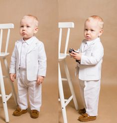 two toddlers dressed in white standing next to each other with their hands on the chair