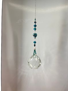 a glass bead hanging from a chain on a white wall with a light bulb