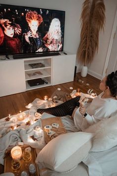 a woman sitting on a couch watching tv with candles in front of her and the television is turned on