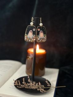 a pair of earrings sitting on top of an open book next to a lit candle