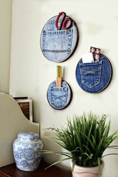 three blue jeans hanging on the wall next to a potted plant and a vase