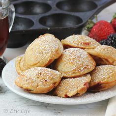 a white plate topped with pastries covered in powdered sugar next to berries and muffin tins