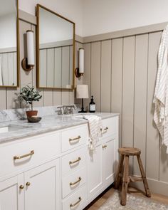 a bathroom with white cabinets and marble counter tops, gold trim on the mirror above the sink