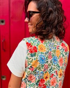 a woman standing in front of a red wall wearing sunglasses and a floral top with short sleeves