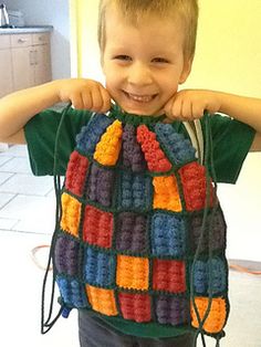 a young boy holding onto a colorful crocheted bag that he made for him