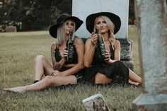 two beautiful women sitting on the ground holding beer bottles