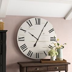 a large clock mounted on the wall above a table with flowers and vases in front of it