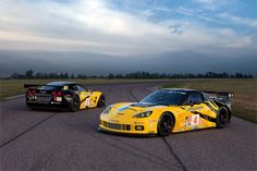 two racing cars on a race track with cloudy skies in the backgrouund