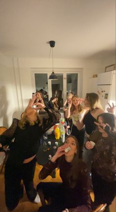 a group of people standing around a kitchen table eating food and drinking beverages from cups