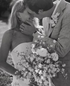 a bride and groom kissing each other in black and white with flowers on the bouquet