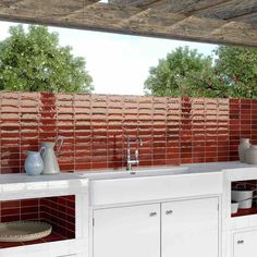 an outdoor kitchen with red tiles on the wall and white cupboards, sink and dishwasher