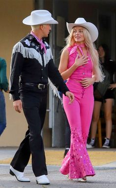 a man in a cowboy hat and pink outfit walking next to a woman with long blonde hair