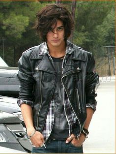 a young man wearing a black leather jacket and jeans standing in front of a parked car