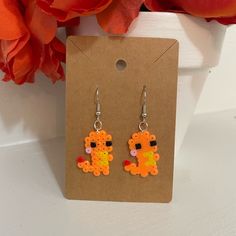 a pair of earrings with an orange and yellow bead design on the front, sitting next to a red flower