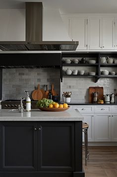 a kitchen with white cabinets and black island in the center is filled with fruits and vegetables