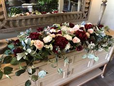 an arrangement of flowers on a dresser in front of a mirror