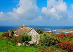 an old stone house sitting on top of a lush green hillside next to the ocean