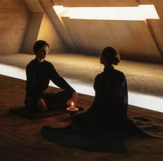 two people sitting on the floor with a lit candle in their hands and looking at each other