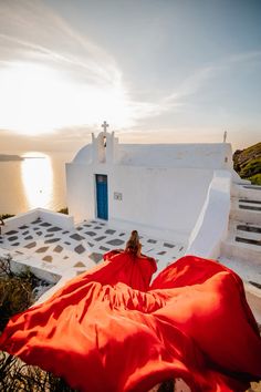 a woman in a red dress is sitting on the steps near a building with a blue door