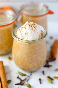 two small jars filled with cinnamon and whipped cream on top of a white surface next to cinnamon sticks