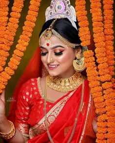 a woman wearing a red sari and gold jewelry with orange garlands around her neck