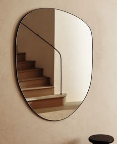 a round mirror hanging on the side of a wall next to a stool and table