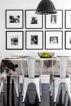 a dining room table with chairs and pictures on the wall behind it in black and white