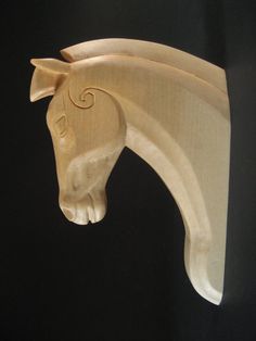 a wooden horse head mounted on the side of a black wall in front of a black background