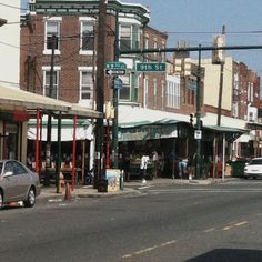 an intersection with cars and people walking on the sidewalk in front of shops, stores, and businesses