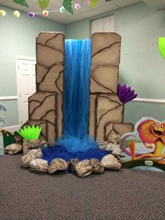 an indoor play area with rocks, water and fake dinosaurs on the ground in front of a waterfall