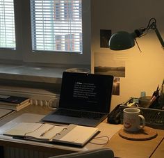 an open laptop computer sitting on top of a wooden desk next to a cup of coffee