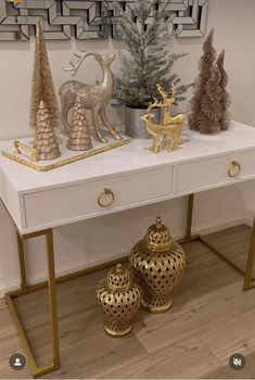 a white table topped with two gold vases next to a christmas tree and other decorations