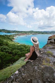 a woman sitting on top of a cliff next to the ocean looking out at the water