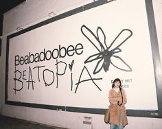 a woman standing in front of a sign that says beaaboobee beattopia