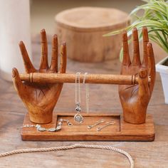 two wooden hands holding up a piece of jewelry on a table next to a potted plant