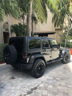 a black jeep parked in front of a building with palm trees on the side of it