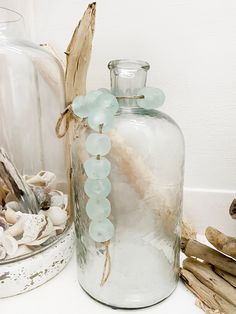 a glass bottle with sea glass on the top next to other shells and driftwood