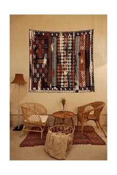 two wicker chairs and a table in front of a wall with a tapestry on it