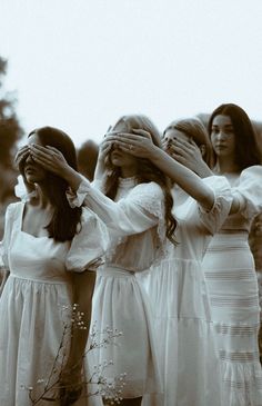 three women in white dresses are covering their eyes