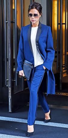 a woman in blue pants and a white top is walking out of a building with her hand on her hip