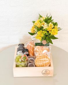 a wooden box filled with assorted snacks and flowers on top of a white table