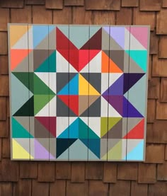 an abstract painting made out of multiple colored triangles on wood paneled wall next to brick building