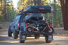 a motorcycle is parked on the back of a truck in the woods with luggage strapped to it