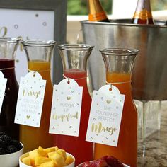 three different types of drinks on a table with tags attached to the bottles and bowls full of fruit